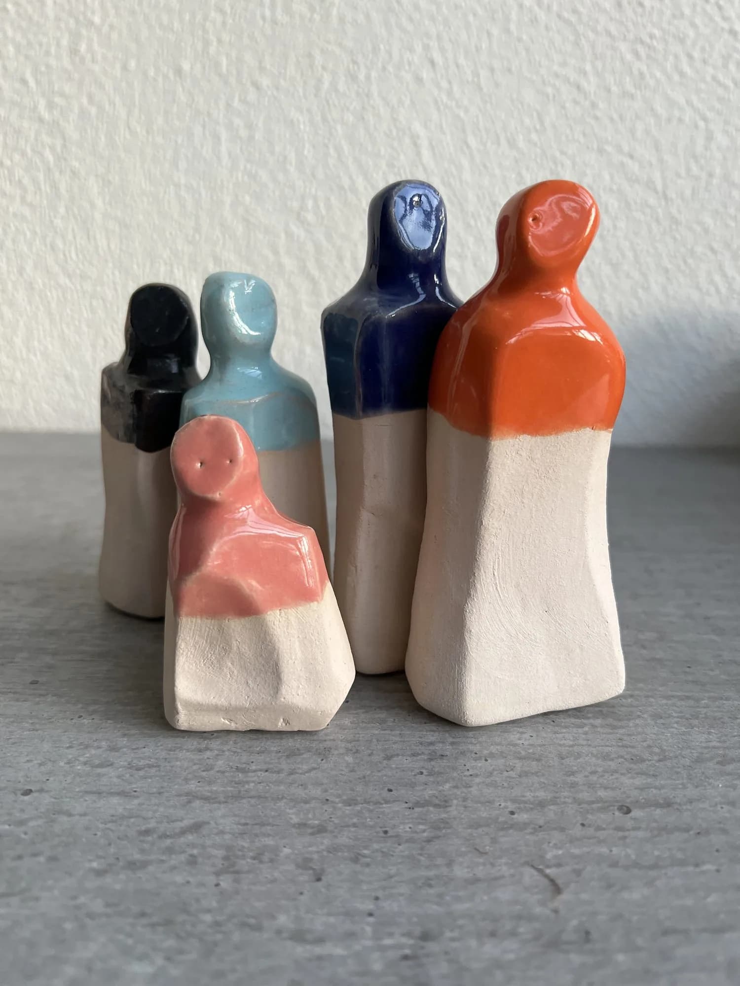 Fünf kleine Keramikfiguren in Violett, Gelb, Weiß, Dunkelblau und Schwarz nebeneinander aufgestellt.