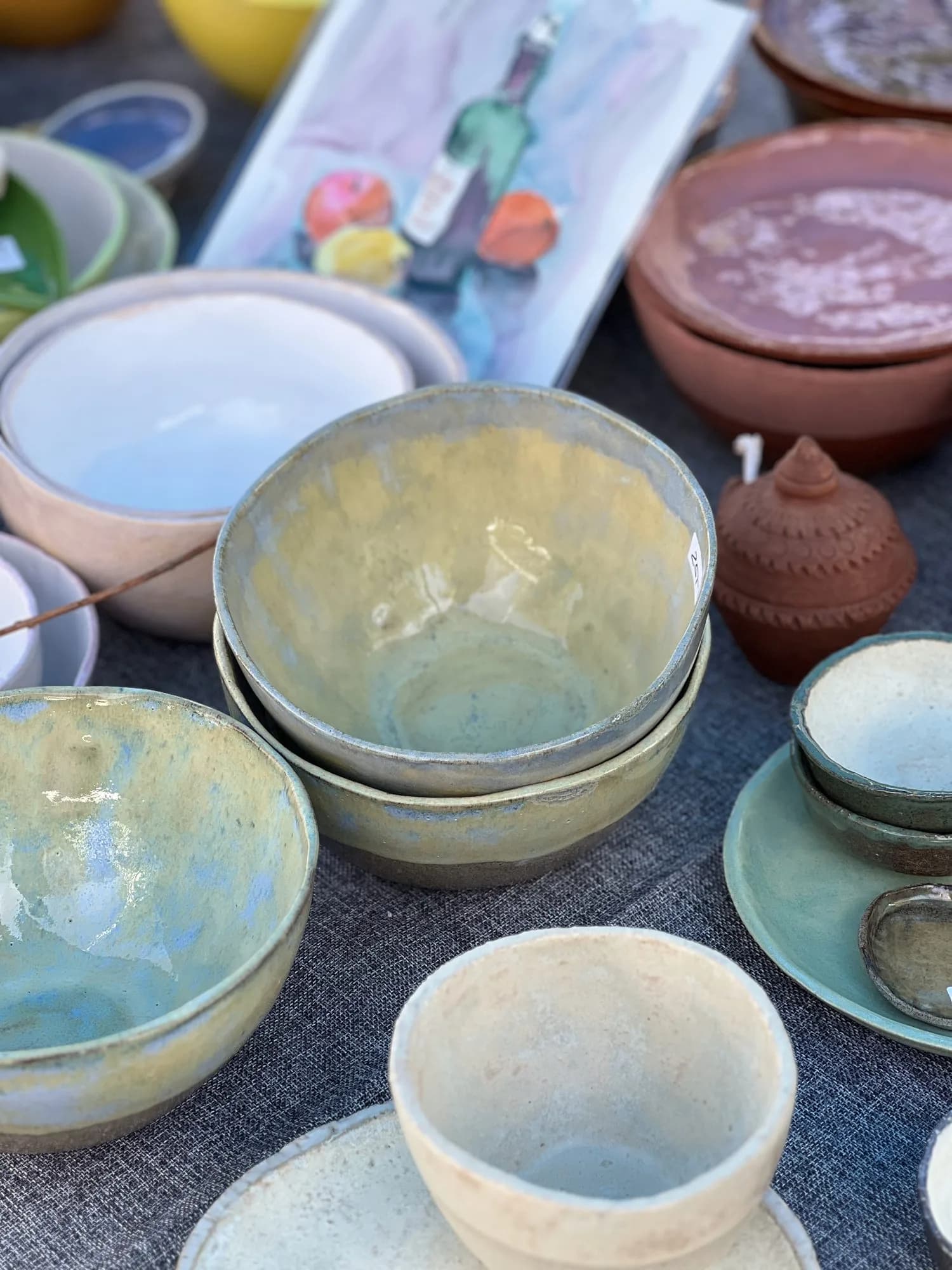 Nahaufnahme eines Marktstands mit gelben, blauen und terrakottafarbenen Keramikschalen und -töpfen.